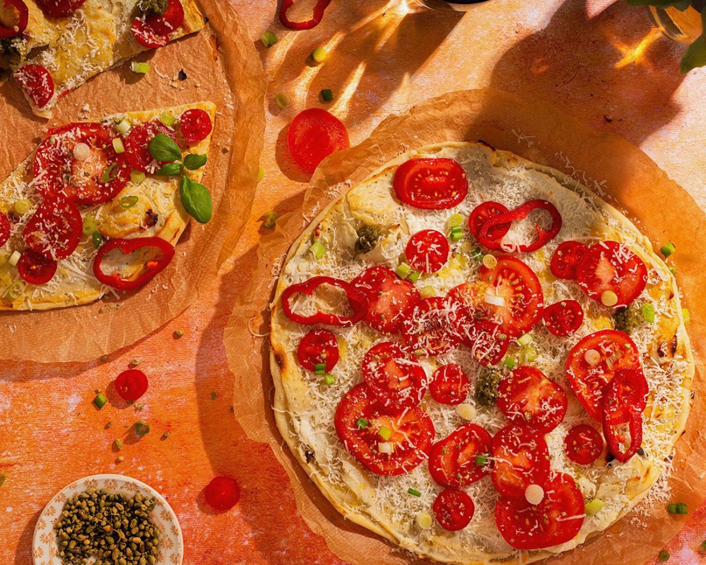Thin pizza with tomatoes, parmesan, pesto and origano in the sunlight.