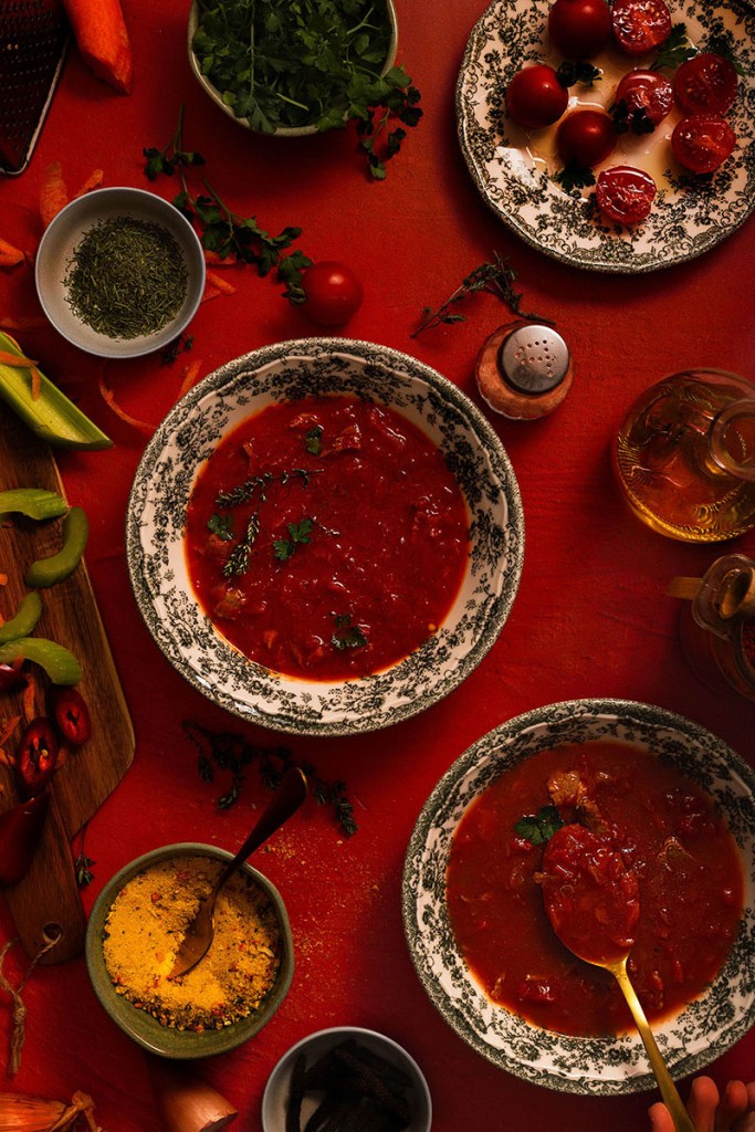 Tomato soup bowl on the table with cherry tomatoes on the red backdrop.