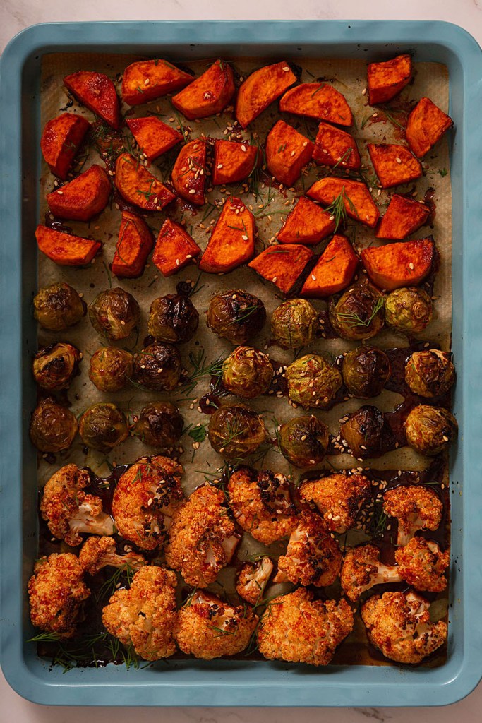 Blue roasting tray with chopped sweet potatoes, Brussel sprouts and cauliflower florets. 