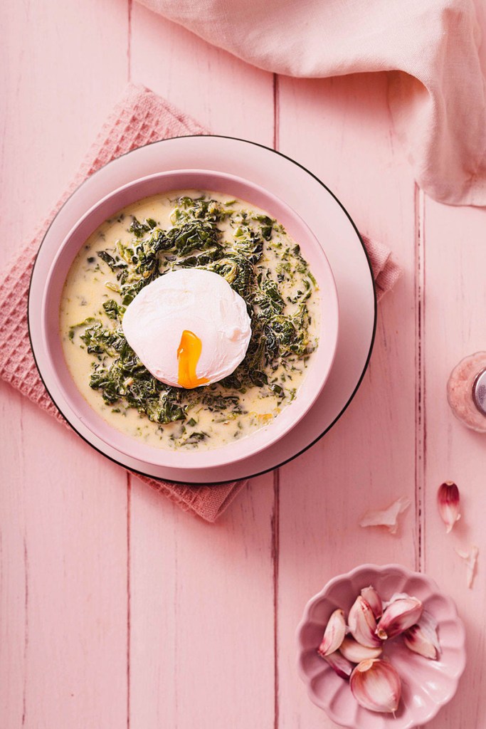 Milky spinach soup with poached egg and garlic on the pink wooden table.