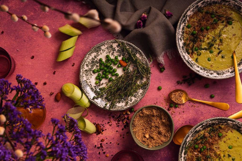 Peas and thyme sprigs on the plate with the peas and leeks soup bowls around.