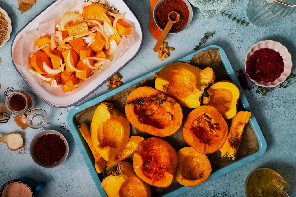 Halved pumpkins, squashes, sweet potatoes and onions on the roasting tray with spices.