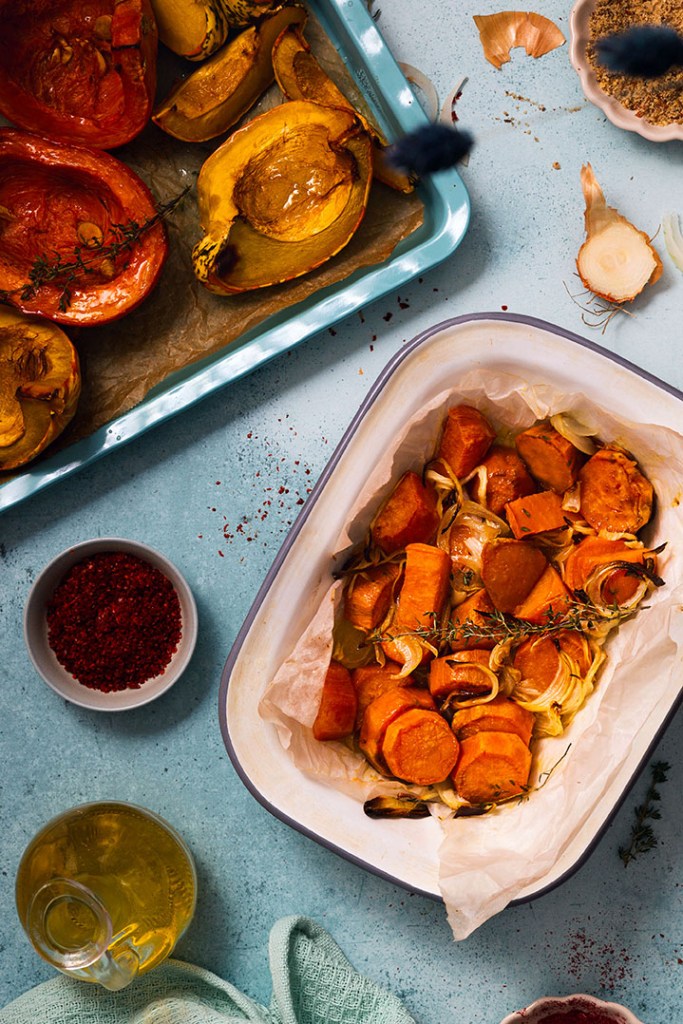 Halved pumpkins, squashes, sweet potatoes and onions on the roasting tray with spices.