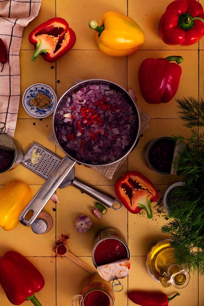 Vegan Stuffed Peppers with Beans and Vegetables with stuffing in the saucepan on the yellow tiles.