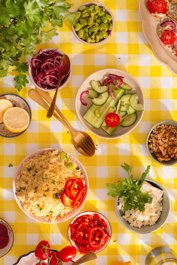 Bulgur salad ingredients: feta, red onions, broad beans, cucumber, tomatoes, chopped walnuts and parsley on the table. 