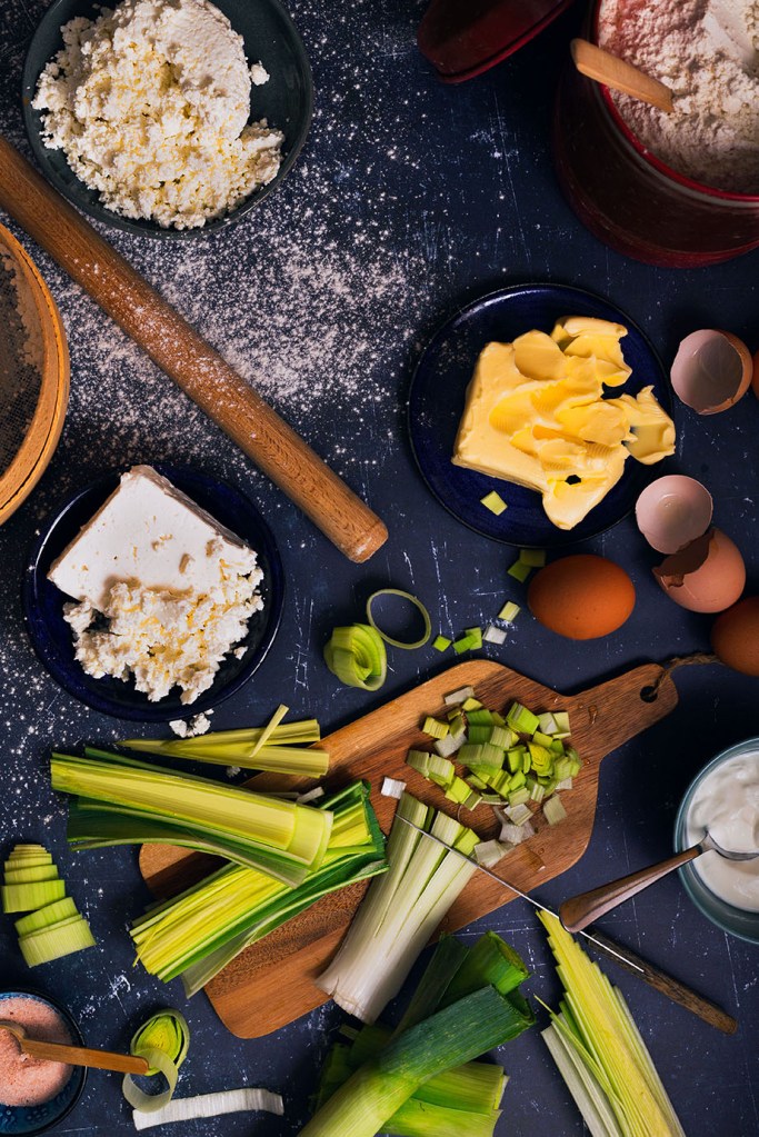 Chopped leek, eggs, butter, and cheese on the table for leek and cheese pie.