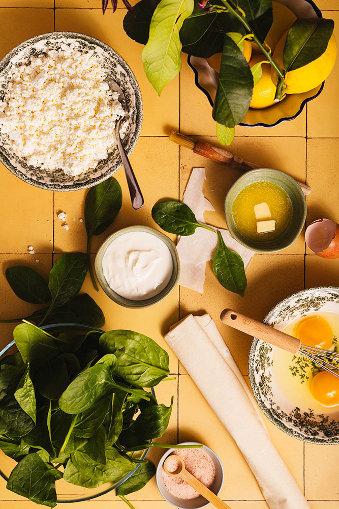 Filo pastry, spinach, eggs, and feta cheese for the pie on yellow tiles..